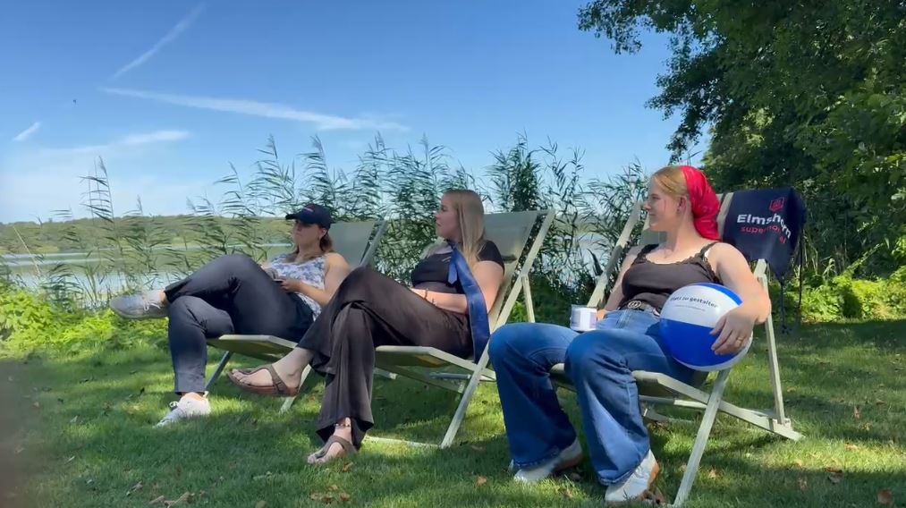Drei Frauen sitzen in Liegestühlen auf einer grünen Wiese und im HIntergrund ist ein See zu erkennen
