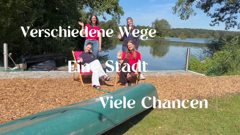 Es sind vier Junge Frau zu sehen, die lächeln und winken und an einem See stehen. Auf dem Bild ist Text zu lesen der lautet Verschiedene Wege, eine Stadt, viele Chancen